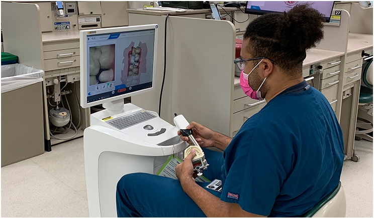 Fourth-year University of Michigan dental student Randon Campbell, wearing a protective mask per pandemic protocols, creates a digital image of typodont teeth with an intraoral scanner in the school's Simulation Lab.
