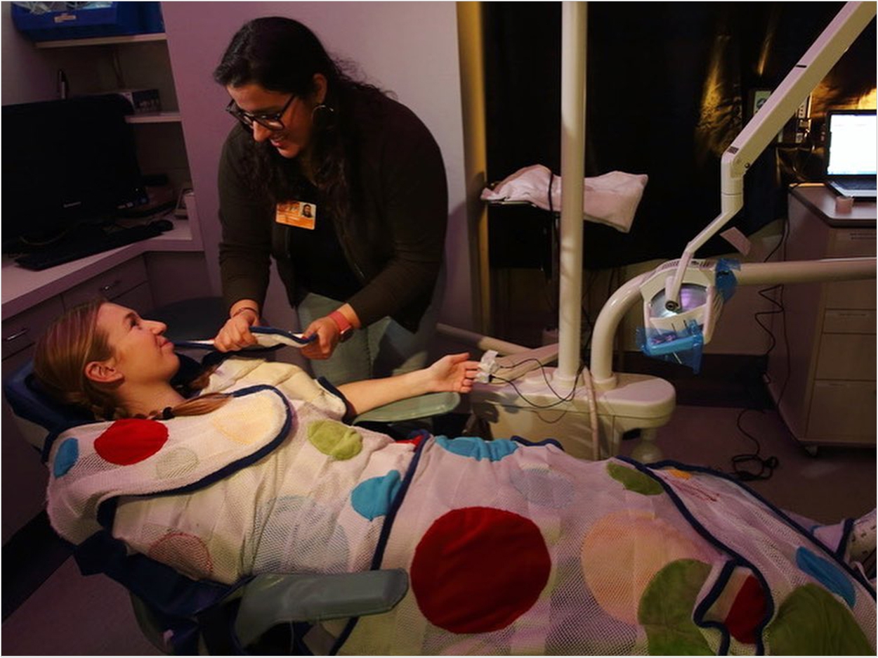 Alterations to the dental environment include low lighting and a weighted blanket that simulates being hugged.